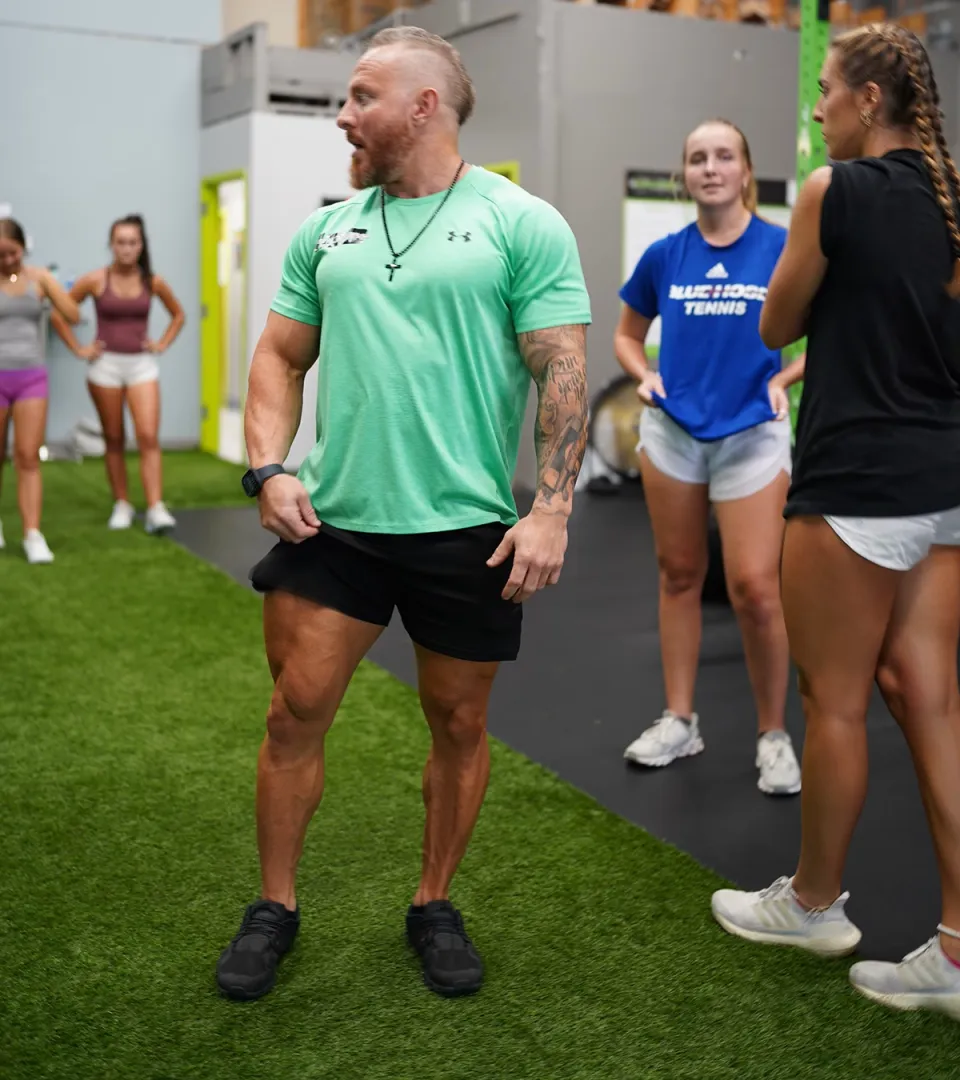 A 123 trainer demonstrating movement to a group of athletes on the turf